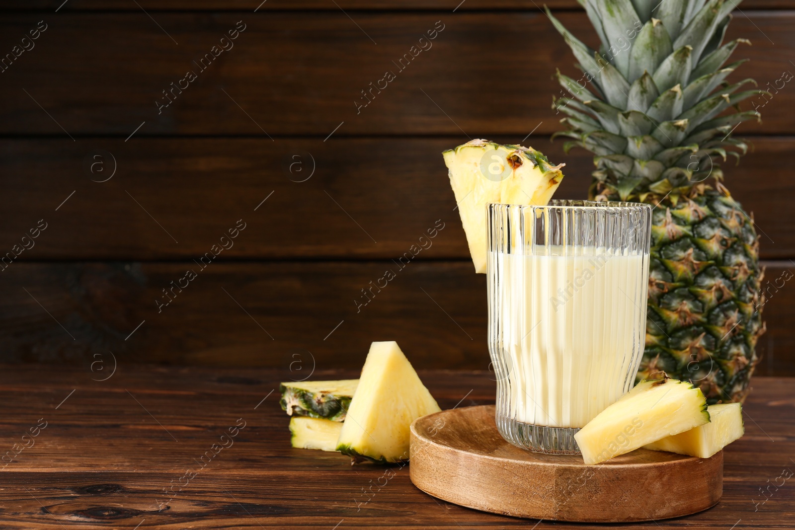 Photo of Tasty pineapple smoothie in glass and slices of fruit on wooden table. Space for text