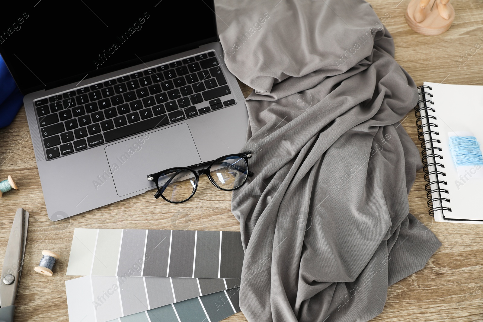 Photo of Laptop, grey fabric and other fashion designer`s supplies on wooden table