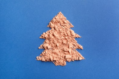 Photo of Christmas tree made with face powder on blue background, top view