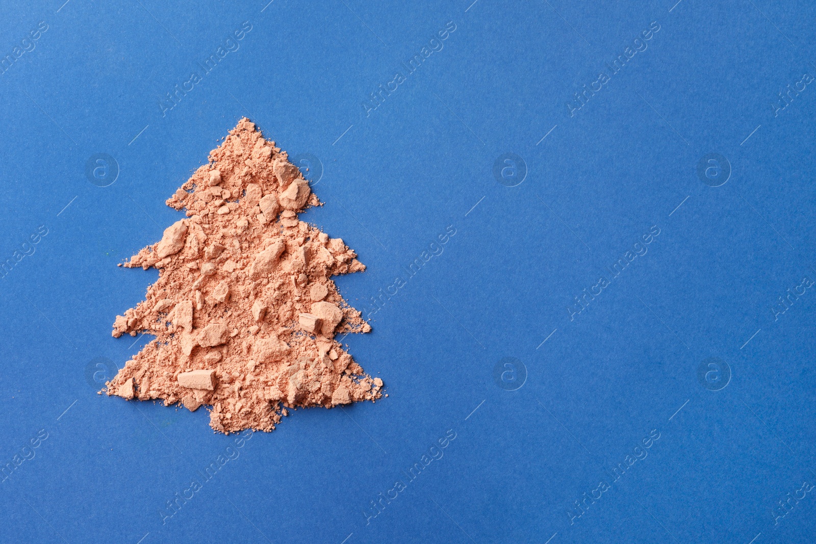 Photo of Christmas tree made with face powder on blue background, top view. Space for text