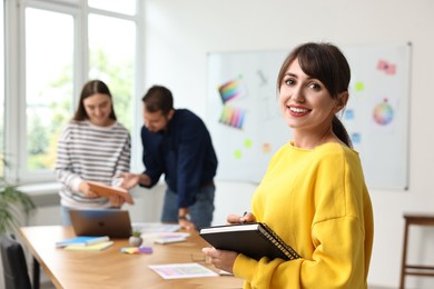 Photo of Portrait of happy young designer with notebook in office