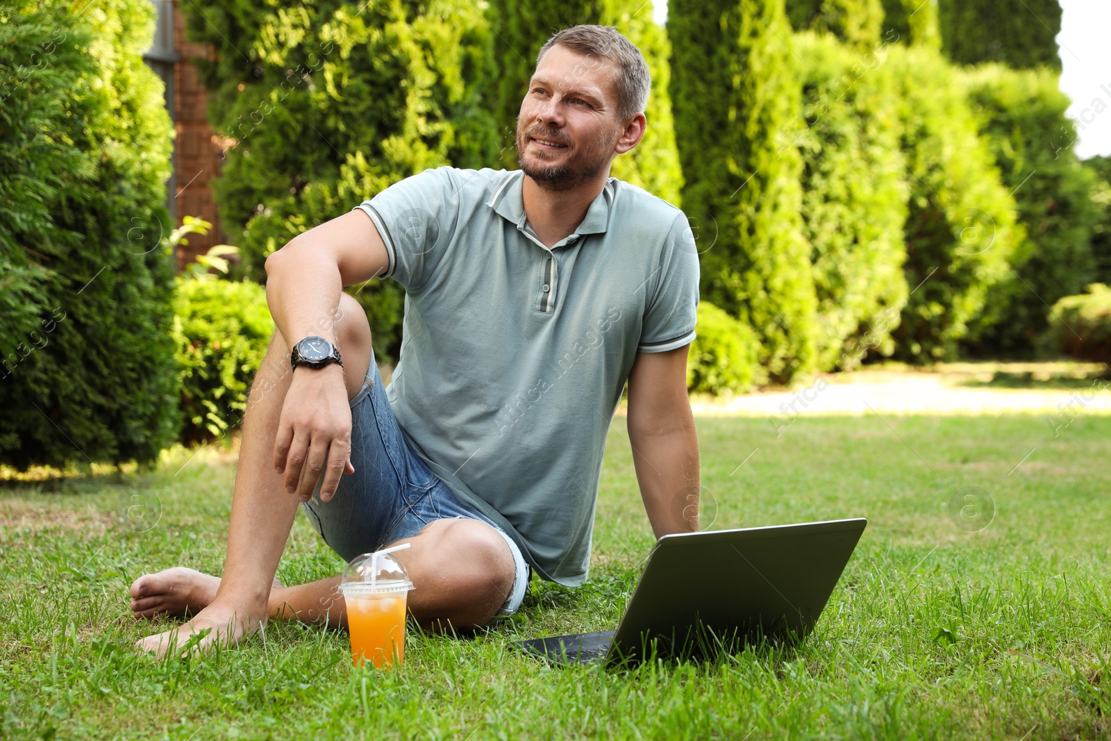 Photo of Man with laptop and juice on green lawn outdoors