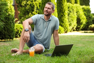 Man with laptop and juice on green lawn outdoors