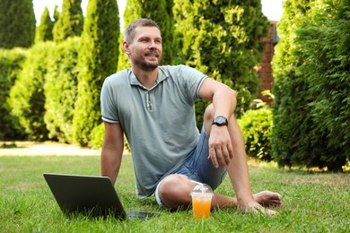 Photo of Man with laptop and juice on green lawn outdoors