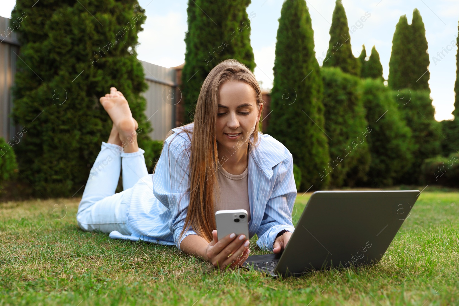 Photo of Woman with smartphone using laptop on green lawn in park