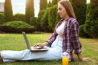 Woman using laptop on green lawn in park