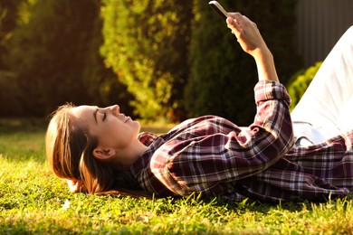 Photo of Woman with smartphone resting on green lawn in park