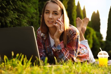 Photo of Woman talking on smartphone near laptop on green lawn in park