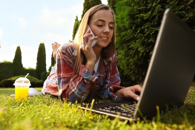 Photo of Woman talking on smartphone near laptop on green lawn in park