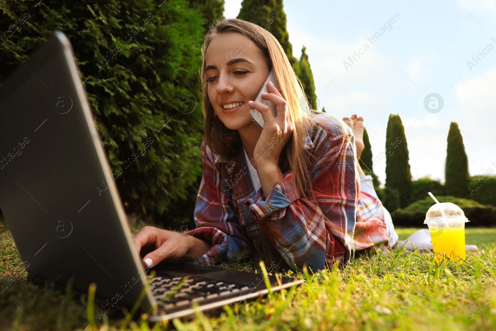 Photo of Woman talking on smartphone near laptop on green lawn in park