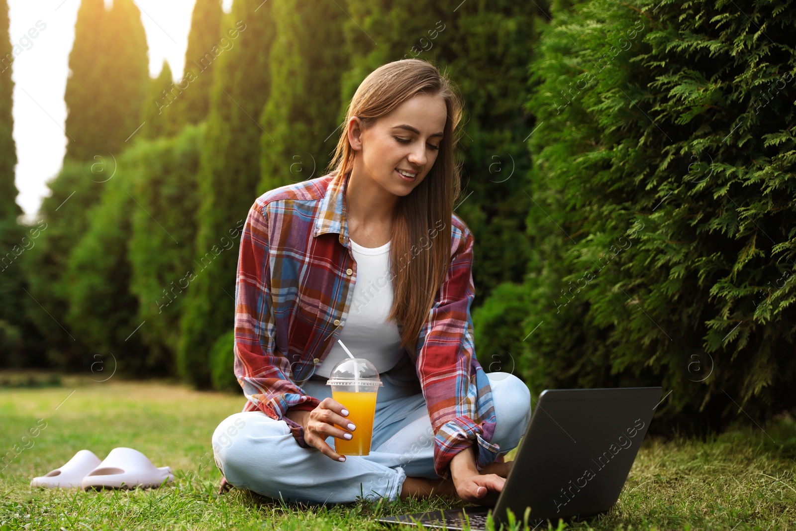 Photo of Woman with juice using laptop on green lawn in park