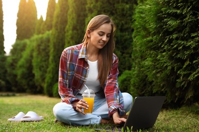 Woman with juice using laptop on green lawn in park