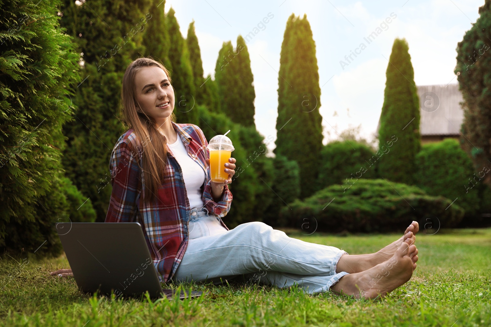 Photo of Woman with juice sitting near laptop on green lawn in park