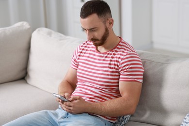 Handsome man using smartphone on sofa indoors