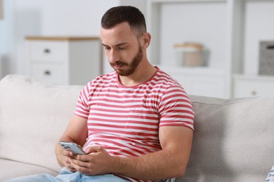 Photo of Handsome man using smartphone on sofa indoors