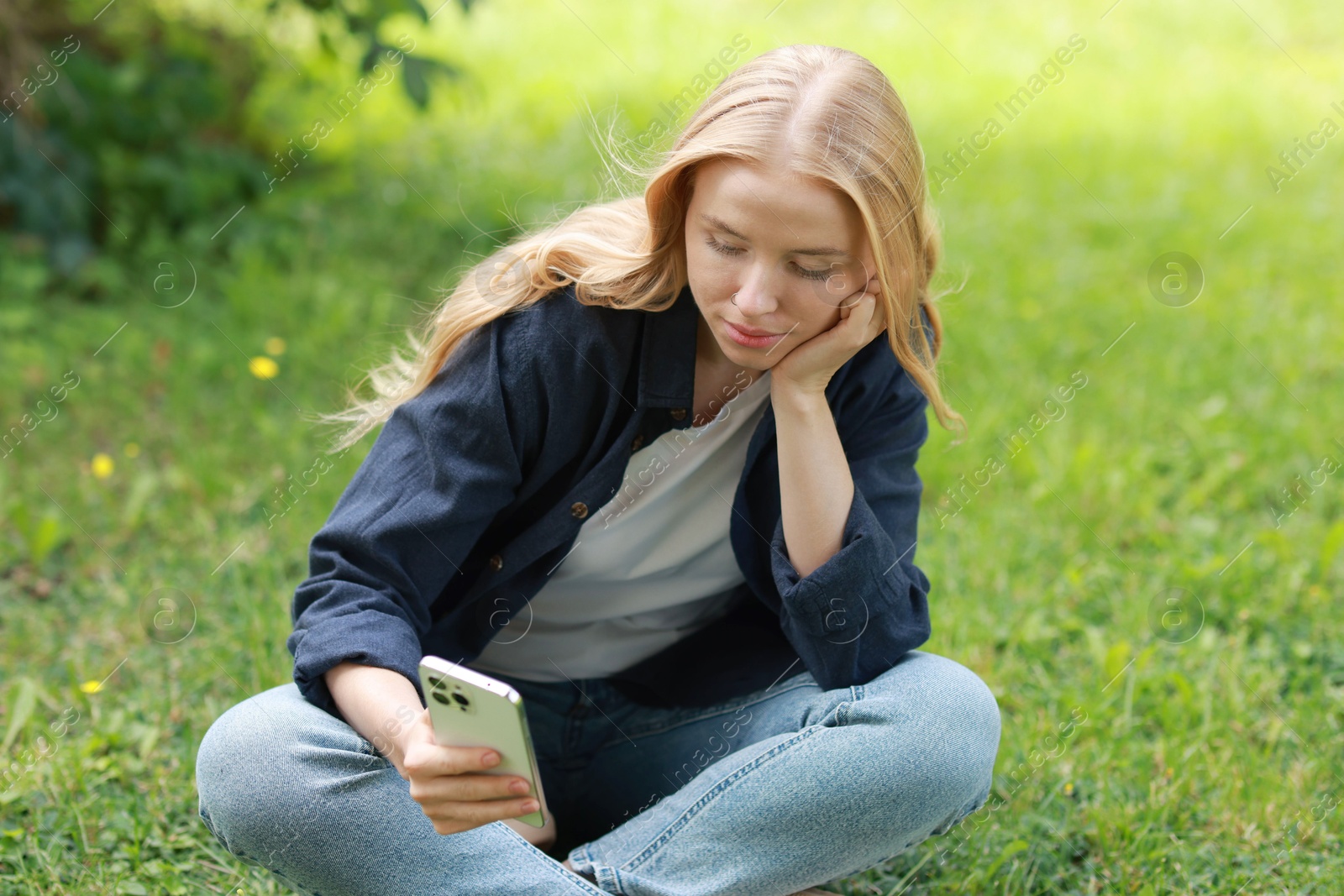 Photo of Beautiful woman using smartphone on green grass outdoors