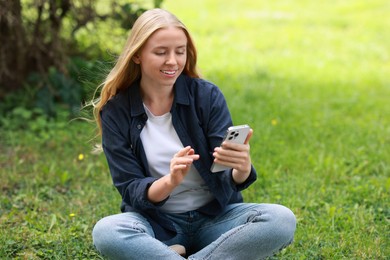 Smiling woman using smartphone on green grass outdoors