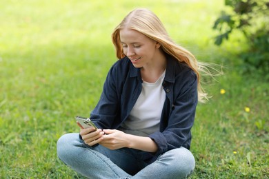 Smiling woman using smartphone on green grass outdoors