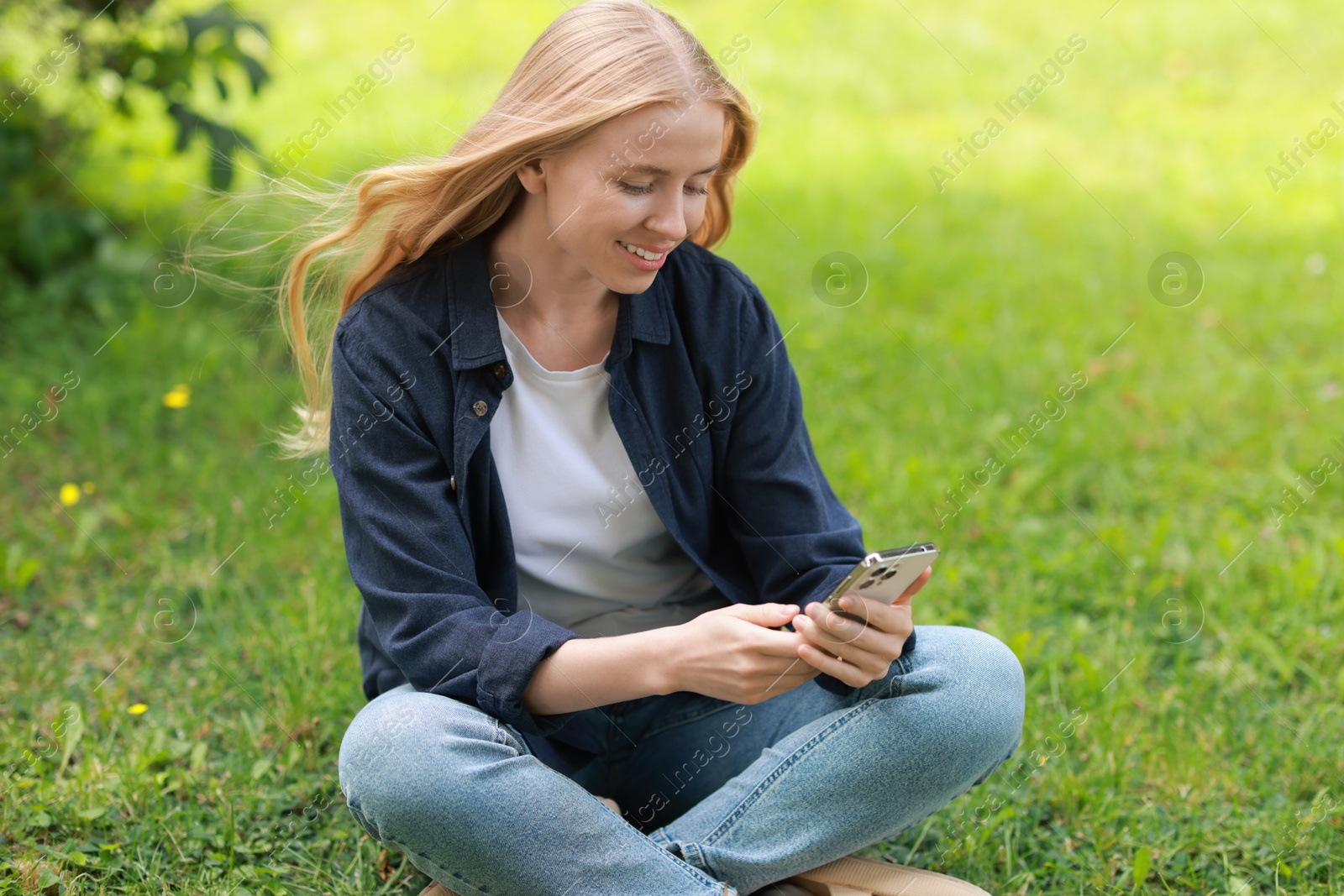 Photo of Smiling woman using smartphone on green grass outdoors