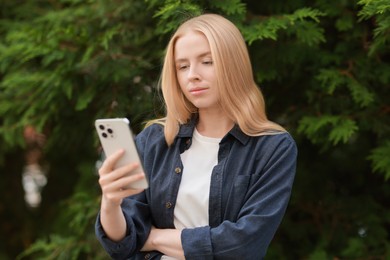 Beautiful woman using smartphone near tree outdoors