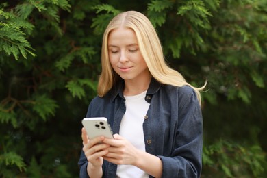 Beautiful woman using smartphone near tree outdoors