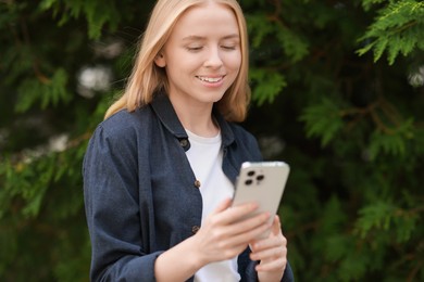 Photo of Smiling woman looking at smartphone near tree outdoors