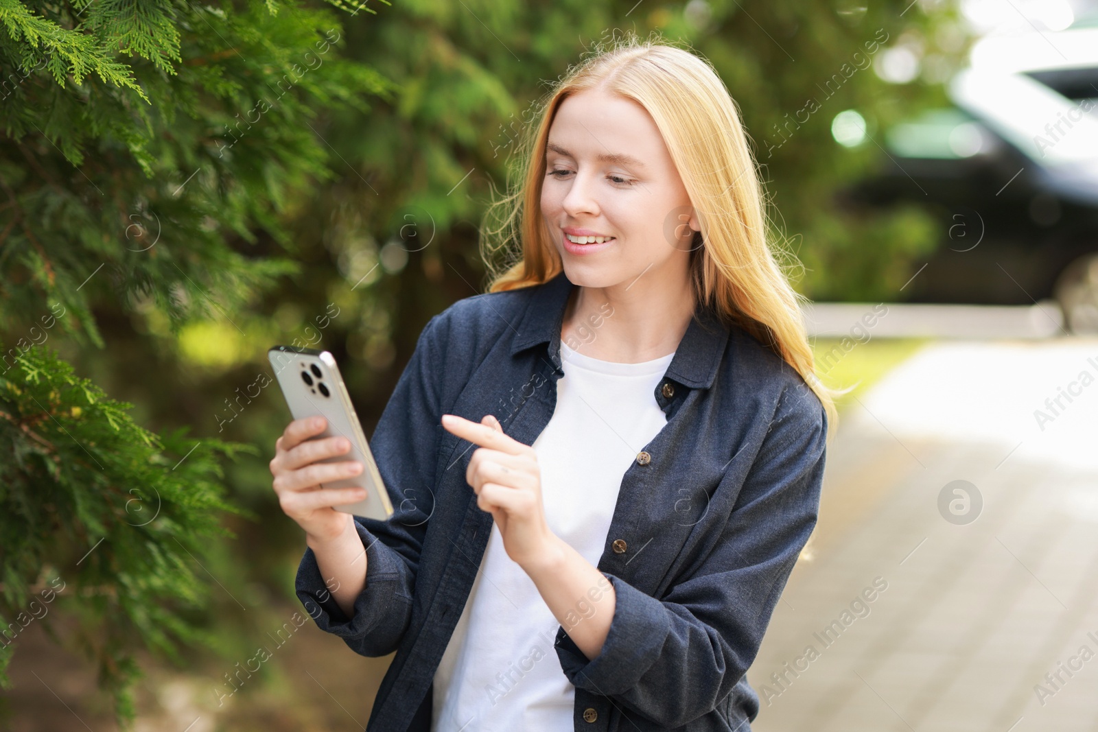 Photo of Smiling woman using smartphone near tree outdoors