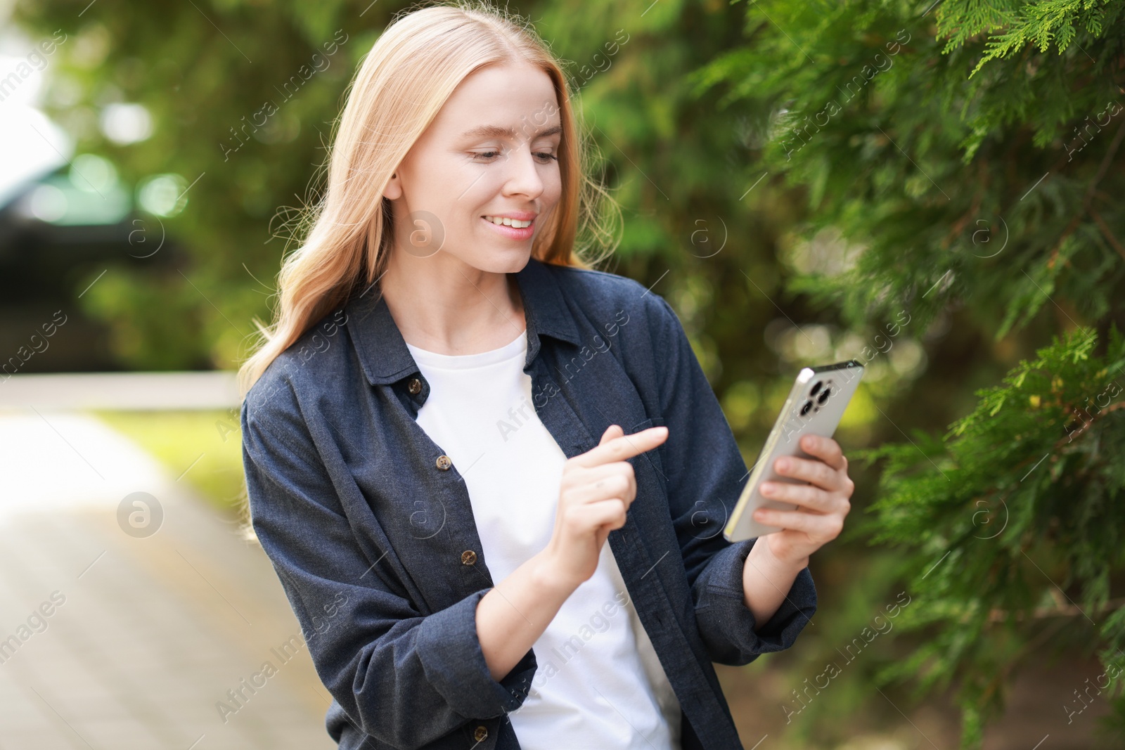 Photo of Smiling woman using smartphone near tree outdoors