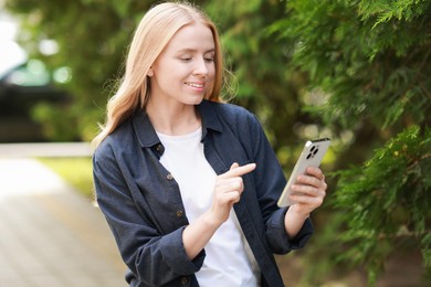 Smiling woman using smartphone near tree outdoors