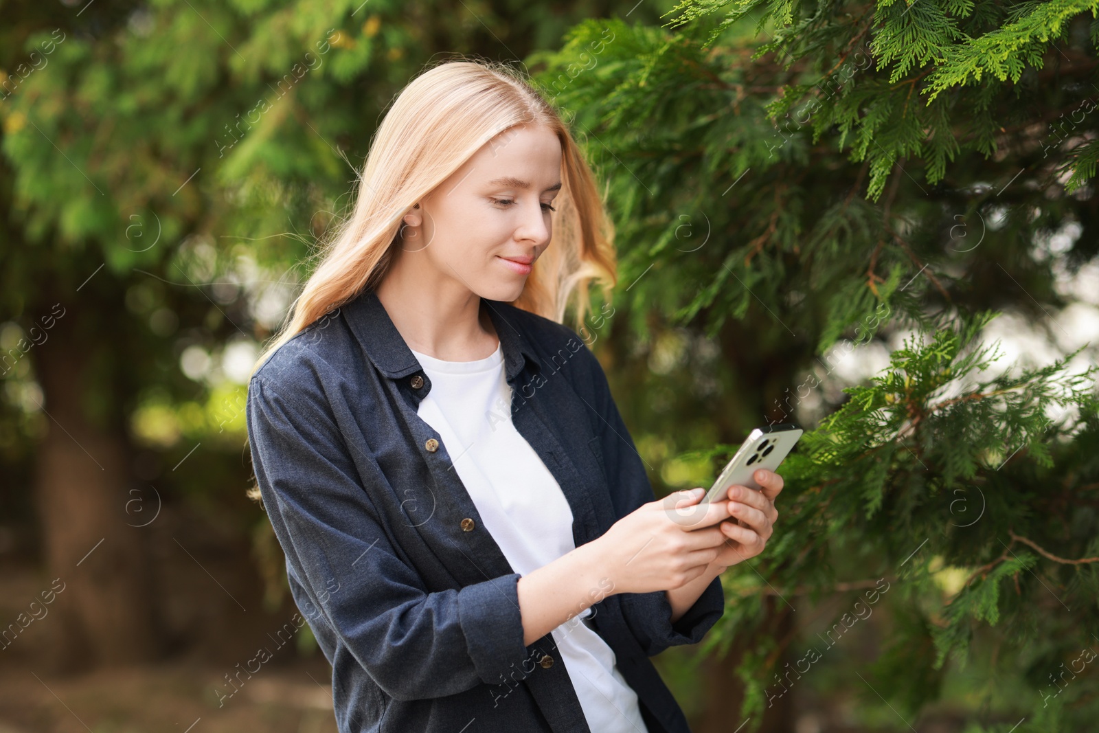 Photo of Beautiful woman using smartphone near tree outdoors