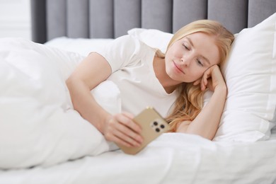 Beautiful woman looking at smartphone in bed