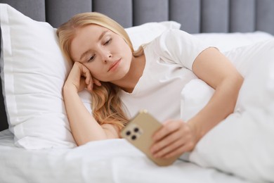 Beautiful woman looking at smartphone in bed