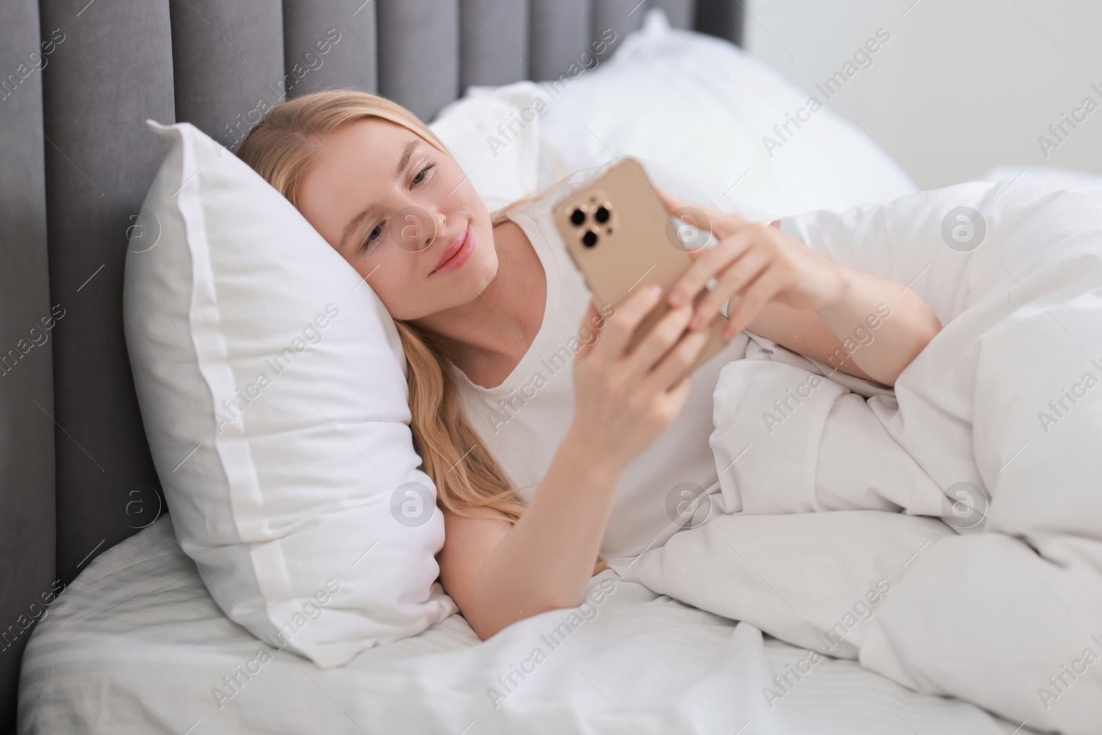 Photo of Beautiful woman looking at smartphone in bed