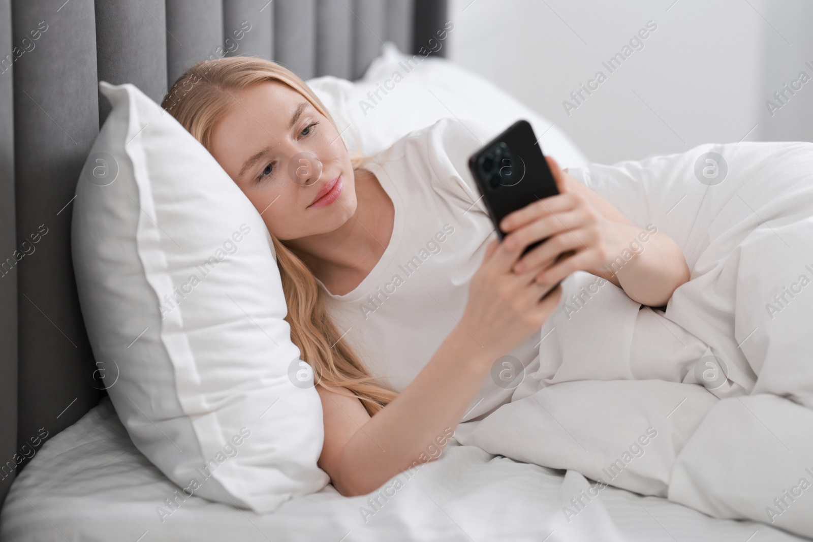 Photo of Beautiful woman looking at smartphone in bed