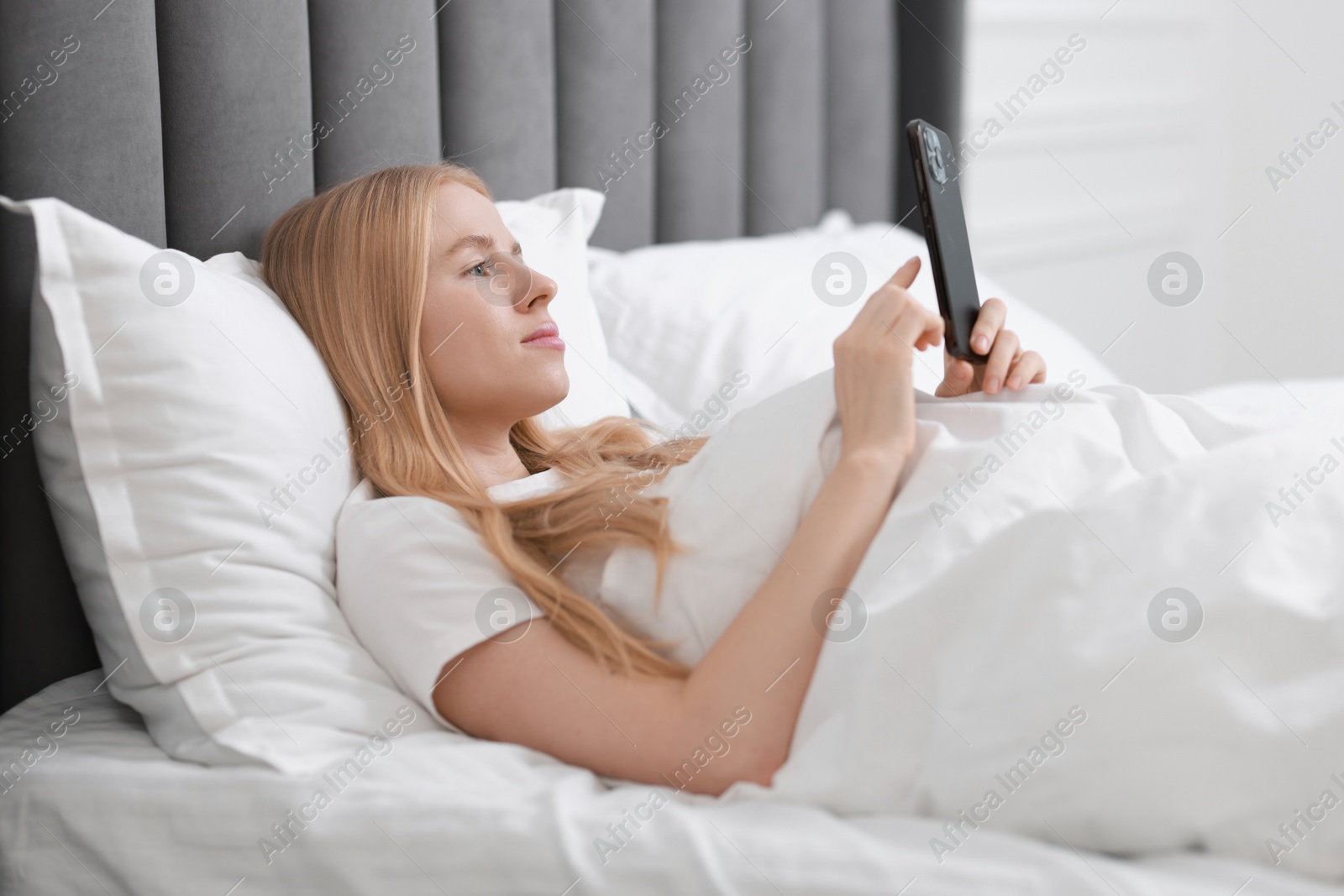 Photo of Beautiful woman looking at smartphone in bed