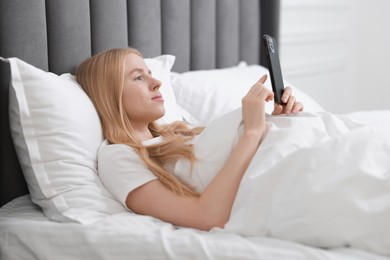 Beautiful woman looking at smartphone in bed