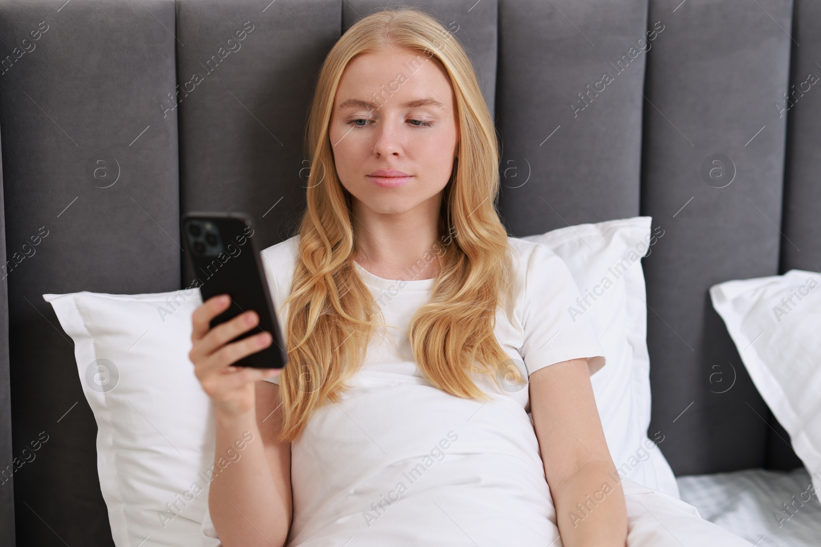 Photo of Beautiful woman looking at smartphone in bed