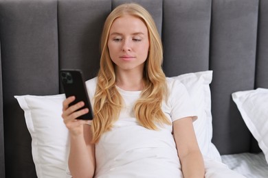 Beautiful woman looking at smartphone in bed