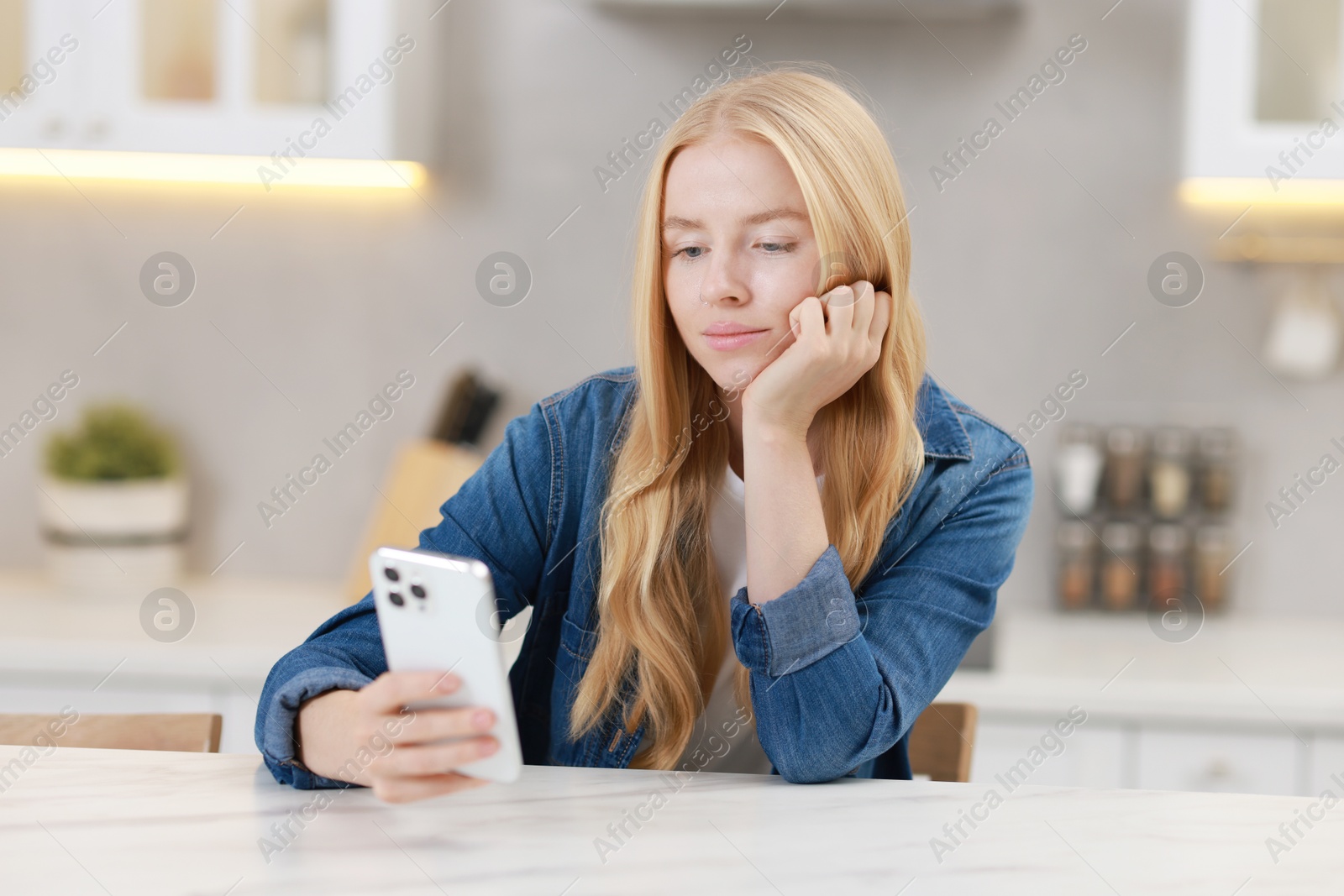 Photo of Beautiful woman using smartphone at white table in kitchen