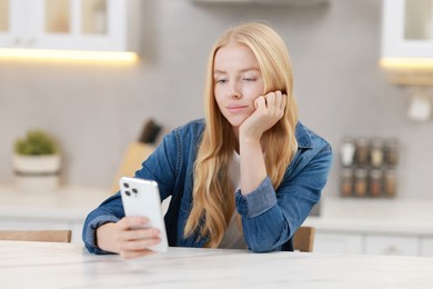 Photo of Beautiful woman using smartphone at white table in kitchen