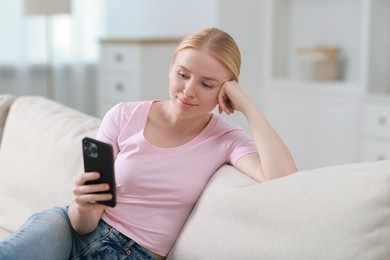 Photo of Beautiful woman using smartphone on sofa indoors