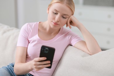 Beautiful woman using smartphone on sofa indoors