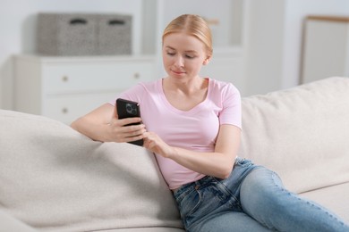 Photo of Beautiful woman using smartphone on sofa indoors