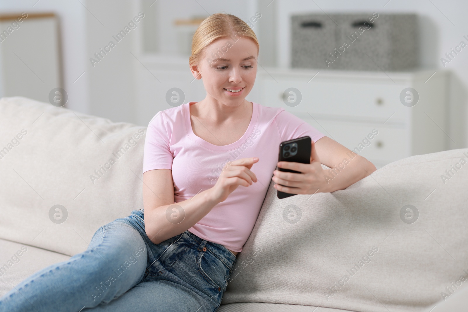 Photo of Smiling woman using smartphone on sofa indoors