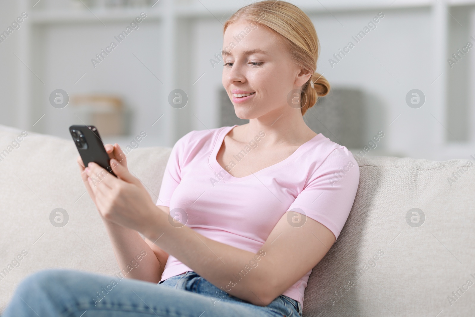 Photo of Smiling woman using smartphone on sofa indoors