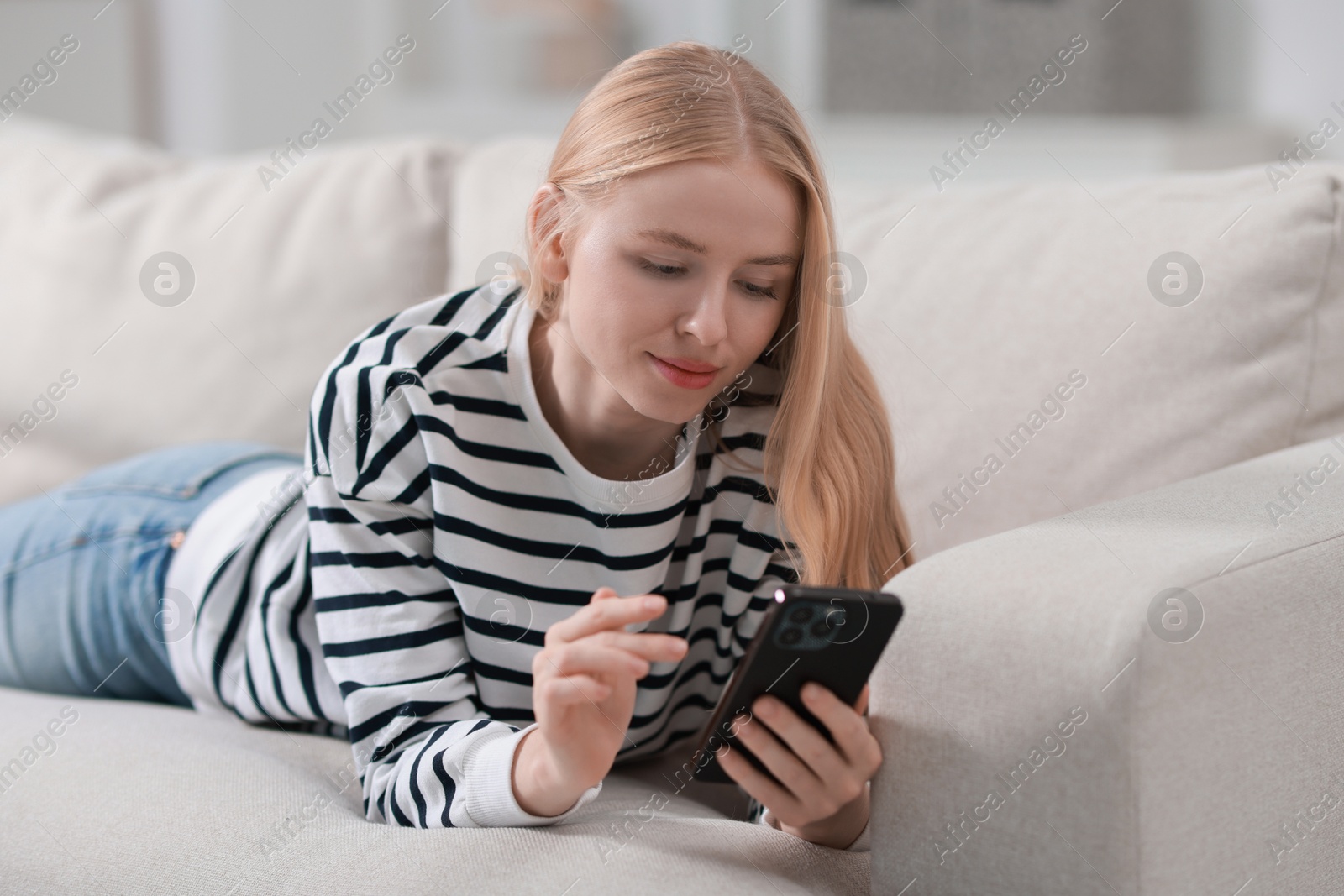 Photo of Beautiful woman using smartphone on sofa indoors