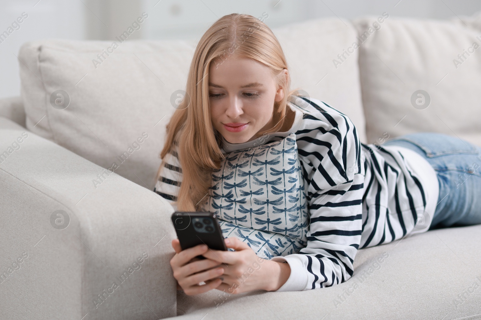 Photo of Beautiful woman using smartphone on sofa indoors