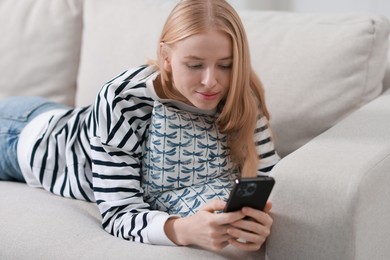 Photo of Beautiful woman using smartphone on sofa indoors