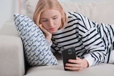 Beautiful woman using smartphone on sofa indoors