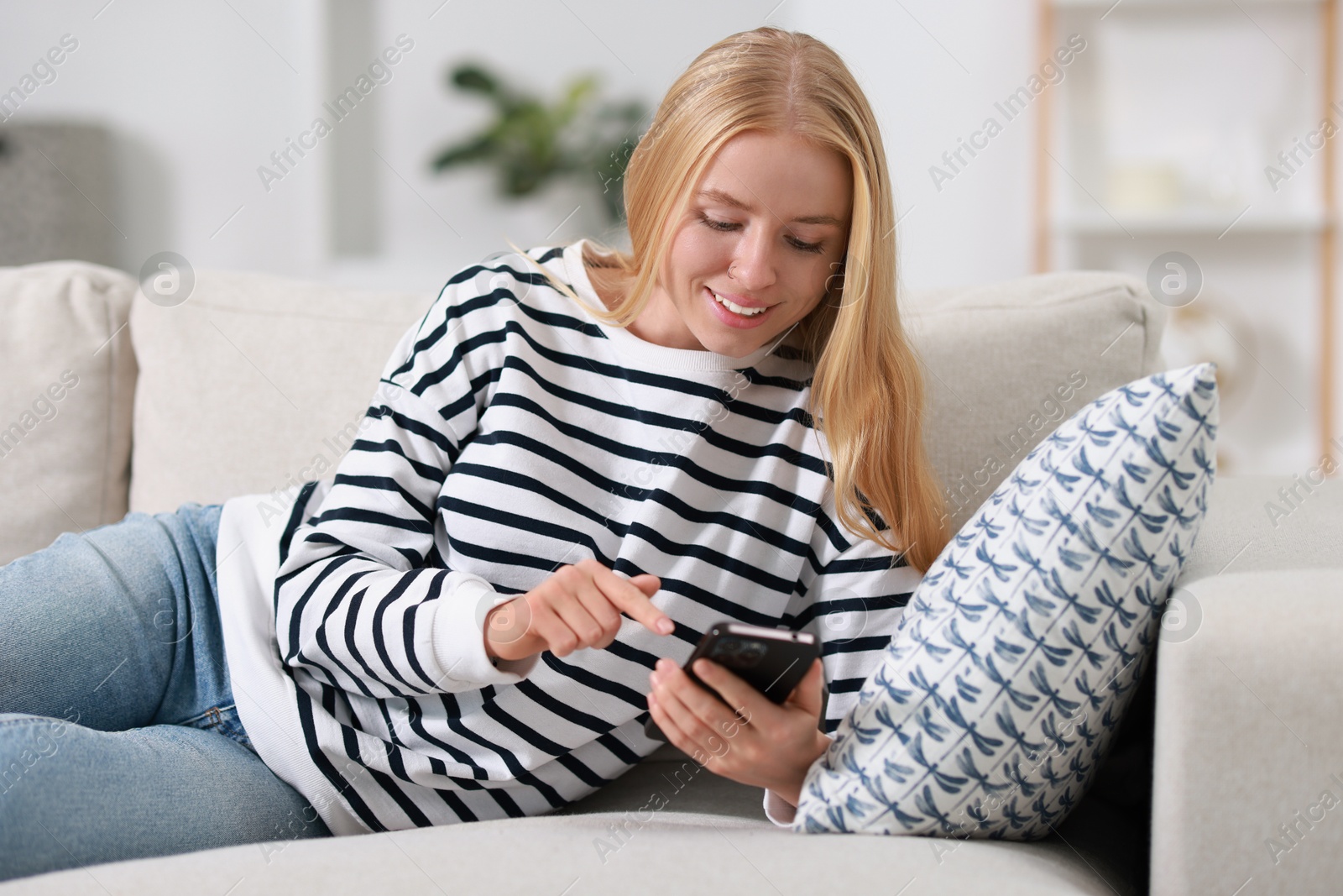 Photo of Smiling woman using smartphone on sofa indoors